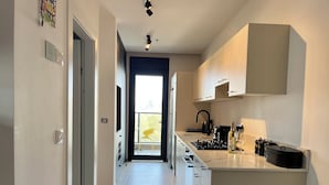 A modern kitchen with white cabinets, a black faucet, and a window overlooking a balcony. - Jerusalem 9 - By Beach Apartments TLV (Bat Yam)