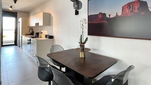A modern kitchen with white cabinets, a dining table with chairs, and a large framed picture on the wall. - Jerusalem 9 - By Beach Apartments TLV (Bat Yam)