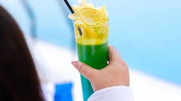 Una persona sostiene un brebaje verde con pajita y decoración de limón junto a una piscina.