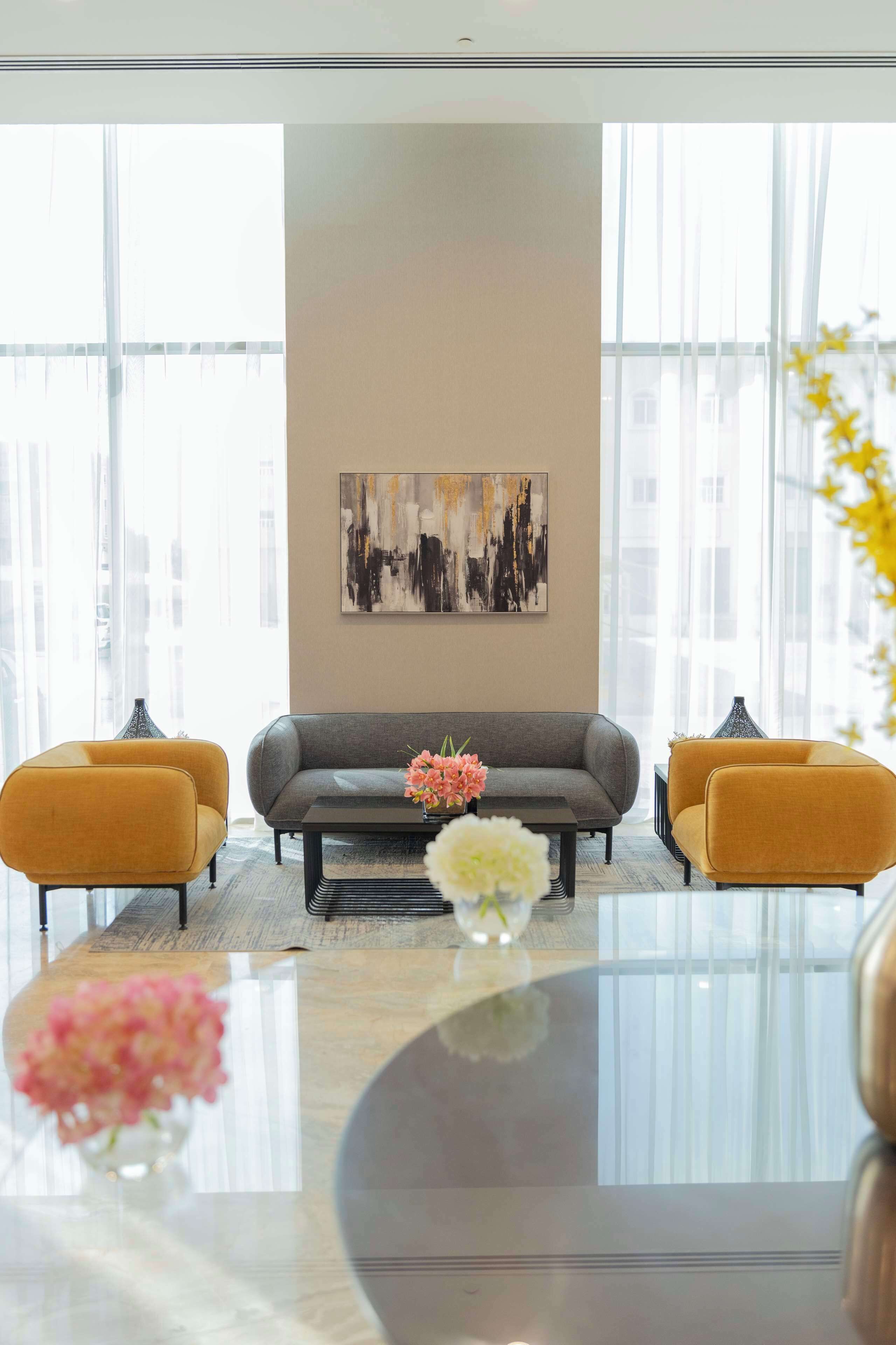 A modern living room with a grey sofa, two mustard-colored armchairs, a coffee table, and a vase with flowers. A large abstract painting is on the wall.