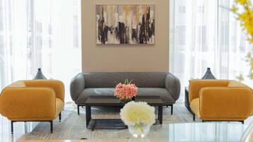 A modern living room with a grey sofa, two mustard-colored armchairs, a coffee table, and a vase with flowers. A large abstract painting is on the wall.