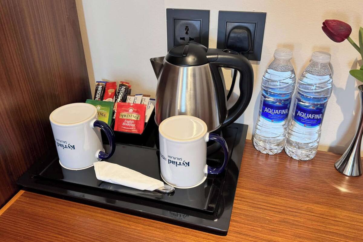 Een dienblad met twee koffiemokken, een theepot en een servetje op een houten tafel.
