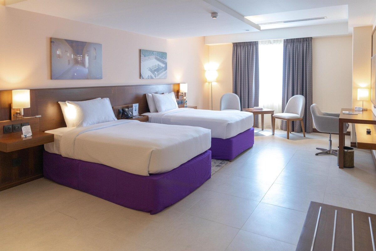 Habitación de hotel con dos camas, un escritorio, una silla y un televisor.