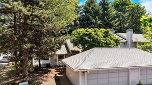 Une maison de plain-pied avec un garage, entourée d’arbres et dotée d’une allée.