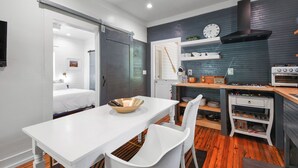 Cocina compacta con una mesa y una silla blancos, una estufa negra y piso de madera.