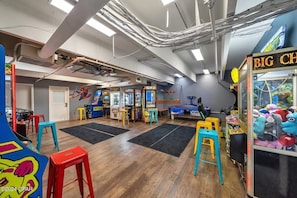 An indoor arcade with various gaming machines, colorful stools, and a claw machine.