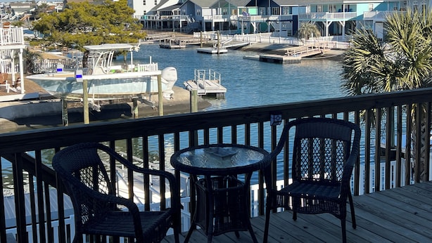 A waterfront property with a dock, a boat, and a view of houses across the water. - THE SANDBAGGER @ OCEAN ISLE (Ocean Isle Beach)