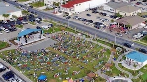 An aerial view of a coastal residential area with multiple apartment buildings, a parking lot, and a community park with playgrounds and a swimming pool. - THE SANDBAGGER @ OCEAN ISLE (Ocean Isle Beach)