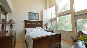A bedroom with a large bed, two bedside tables, a dresser, a chair, and a window with a view of greenery. - Stunning Panoramic Views of Mtns & Lake (Eden)