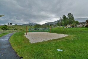 A gravel volleyball court with a blue net, surrounded by green grass and trees, with a path leading to it. - Stunning Panoramic Views of Mtns & Lake (Eden)