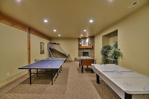 A room with a ping pong table, foosball table, and a fireplace.