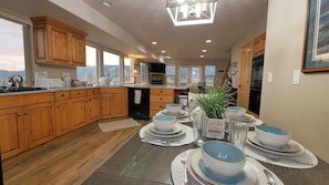 A modern kitchen with wooden cabinets, a dining area set for four, and a view of the mountains through large windows.