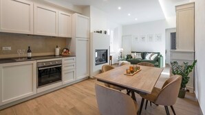Una cocina moderna con armarios blancos, un comedor con mesa y sillas de madera, y una sala de estar con un sofá verde y obras de arte en la pared.