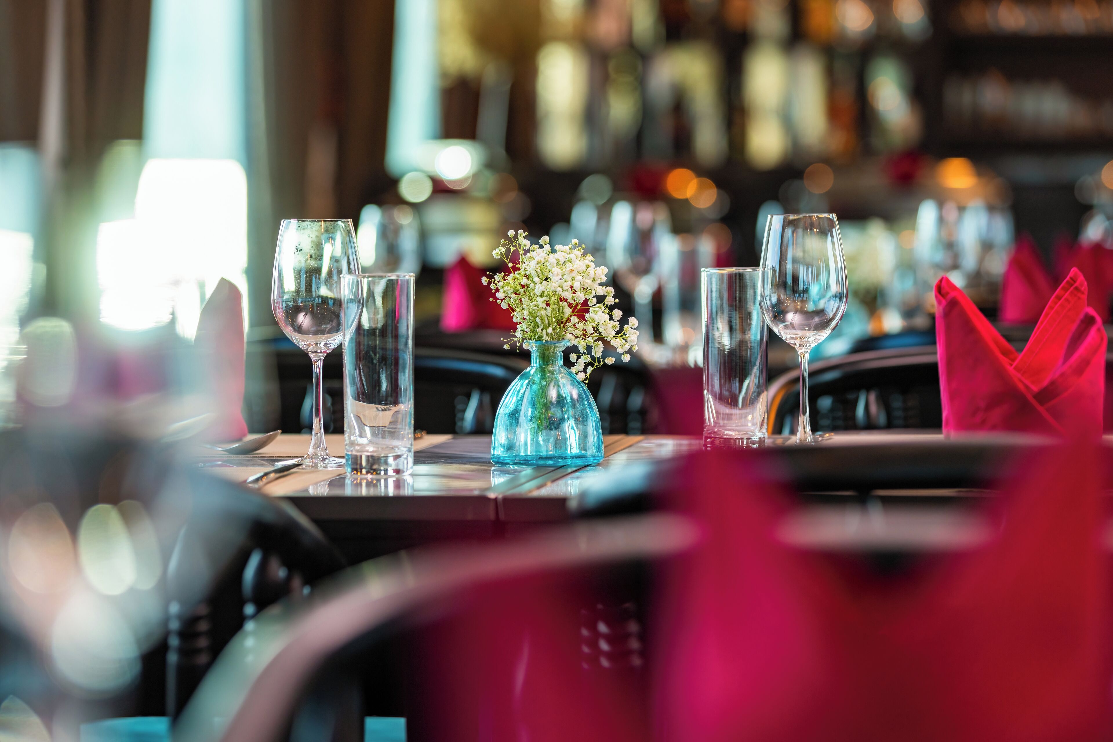 Une table à manger dressée avec des verres à vin, un vase de fleurs et des serviettes rouges.