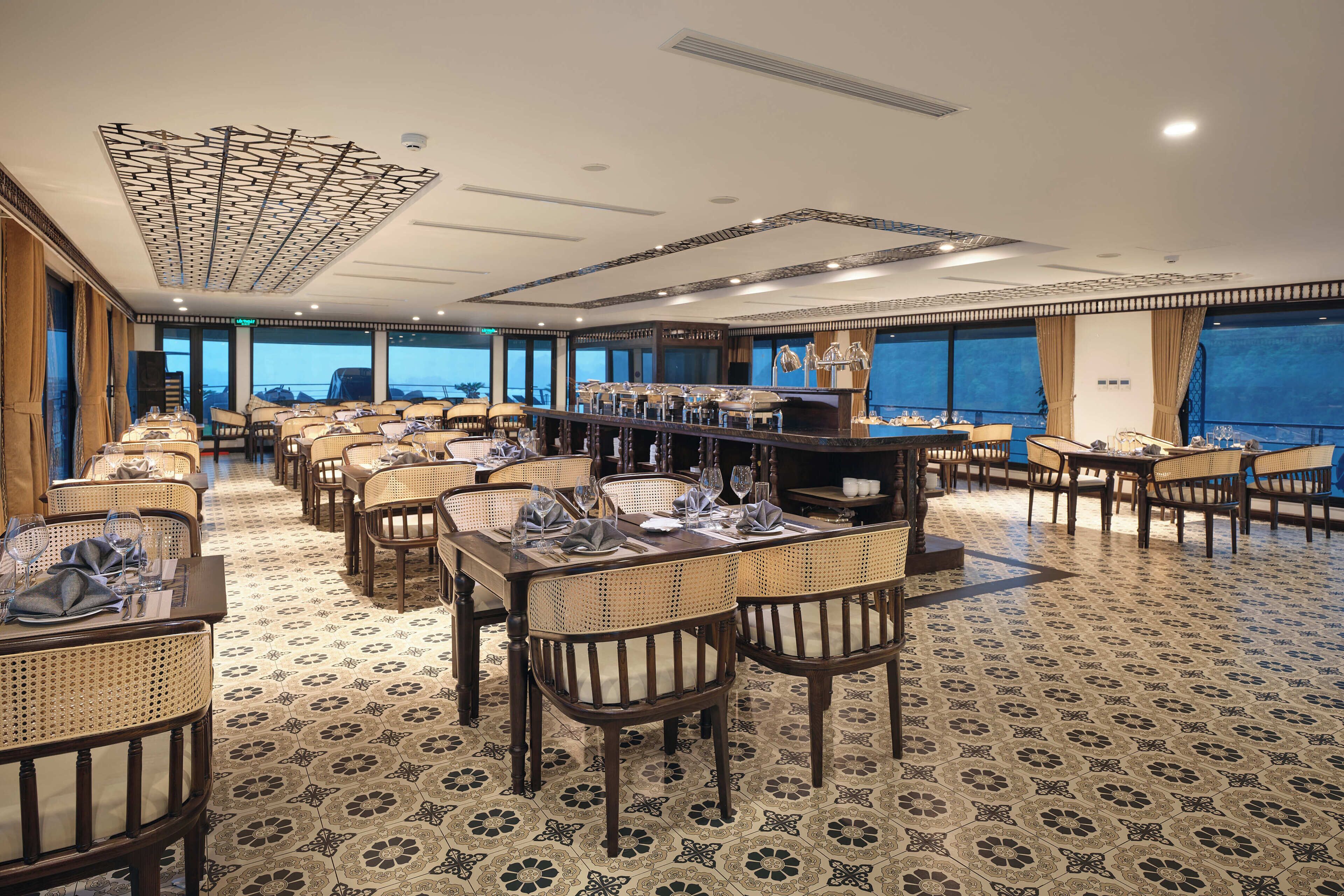 A restaurant with multiple tables and chairs, large windows, and a patterned floor.