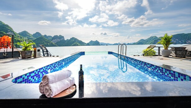 Una piscina con piastrelle blu, una bottiglia e degli asciugamani su una terrazza con vista sulle montagne e sull'acqua.