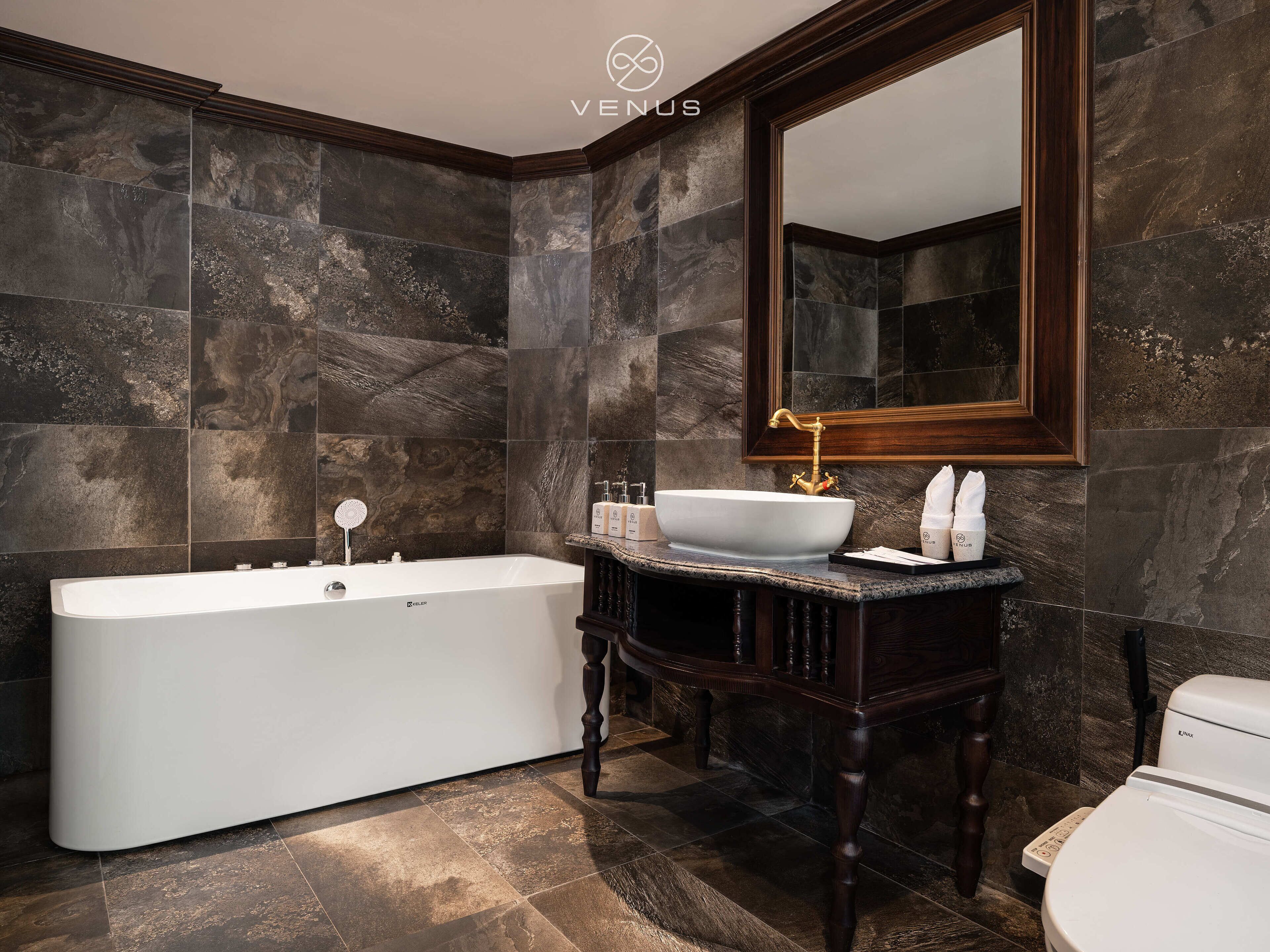 Une salle de bain moderne avec une baignoire sur pieds, un grand miroir et des murs recouverts de marbre foncé.