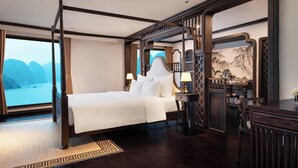 Un letto a baldacchino con vista su un corpo d'acqua e montagne, una scrivania con una lampada, e un decoro murale in stile tradizionale.