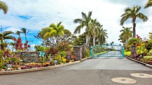 A gated entrance to Kapahulu Bay Villas with a sign, palm trees, and tropical plants. - Contemporary cool with endless Ocean views (Lahaina)