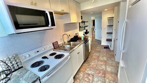 Una cocina con gabinetes blancos, estufa, microondas y refrigerador.