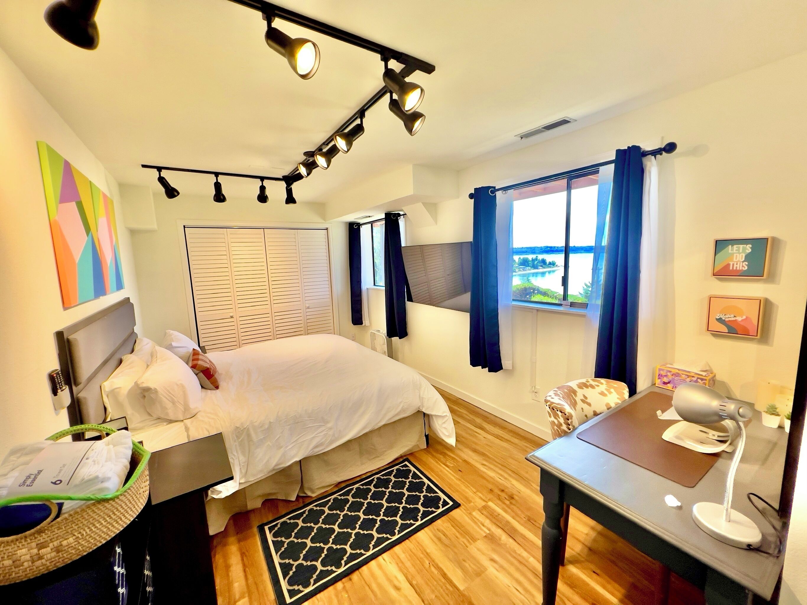 A modern bedroom with a bed, bedside table, desk, and a view of the outdoors.