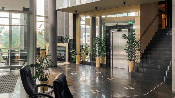 Un hall d’entrée moderne avec un comptoir d’accueil, des plantes en pot, un escalier et une entrée en verre.