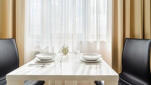 Une table à manger dressée avec des assiettes, des verres et des couverts, placée devant une fenêtre ornée de rideaux légers.
