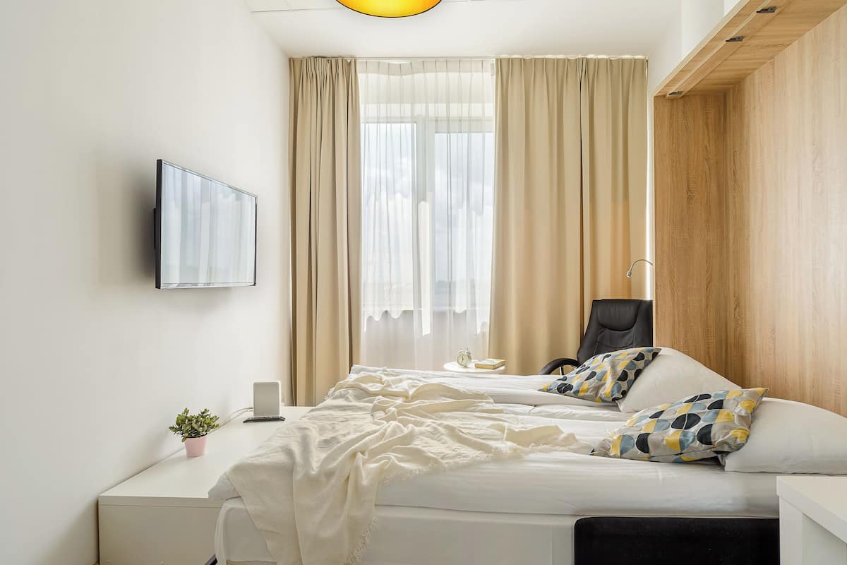 A modern hotel room with a bed, a desk, a chair, a TV, and a window with curtains.