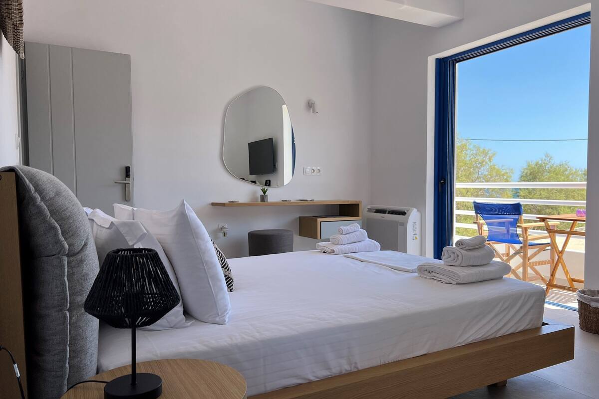 A modern hotel room with a large bed, a round table, a TV, and a balcony with a view.