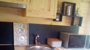 A compact kitchen with wooden cabinets, a stainless steel sink, a microwave, and a small refrigerator. - ROULOTTE ANAÏS A LA CHAUM'YER (GRANDCOURT)