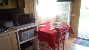 A compact kitchen with a microwave, storage shelves, and a dining table set for four. - ROULOTTE ANA ÏS A LA CHAUM'YER (GRANDCOURT)