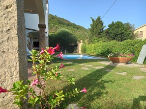 A pool area with a view of a mountain, surrounded by greenery and a stone pathway. - Apartment I Gelsomini # (Tanaunella)