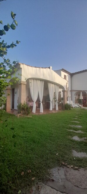 A building with a covered patio area, a grassy lawn, and a pathway leading to the entrance. - Apartment I Gelsomini # (Tanaunella)