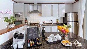 Una cocina moderna con armarios blancos, un refrigerador de acero inoxidable, una cafetera y un cuenco de frutas en la encimera.