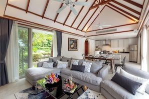 A modern living room with a sectional sofa, a coffee table with magazines, and a view of the kitchen and garden.