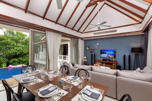 Un salon moderne comprenant un coin repas, un téléviseur et donnant sur la piscine.