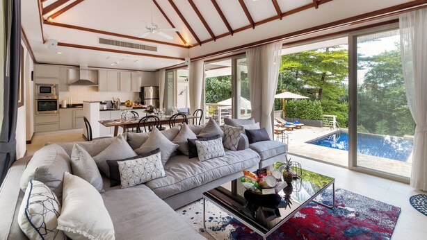 Una sala de estar moderna con un sof á grande, un comedor y vistas a una piscina.