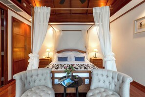 Una cama con dosel y cortinas blancas, cabecera de madera y mesita de noche con una revista y un florero.
