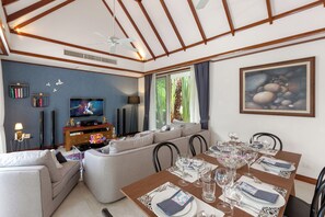 Una sala de estar moderna con televisor, sofá, mesa de comedor preparada para seis personas y ventilador de techo.
