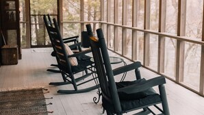A porch with rocking chairs and a glass table, overlooking a wooded area. - A River Runs Through It: Right on the River (Sevierville)