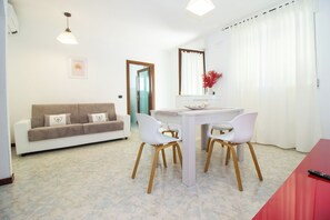 A modern living room with a white sofa, two white chairs, a dining table, and a red table.