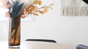 A round wooden table with a vase of dried flowers and a black chair. - MIKLAT Tranquil & Charming Apt near Hayarkon Park by FeelHome (Tel Aviv - Jaffa)