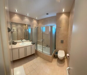A modern bathroom with a large mirror, a shower enclosure, a toilet, and a sink.