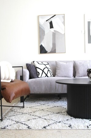 Una sala de estar moderna con un sofá gris, un sillón de cuero marrón, una mesa de centro negra y una alfombra estampada.