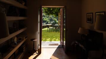 A room with a wooden floor, a bookshelf, a desk, and a chair. There is a door leading to an outdoor area with a table and chairs.
