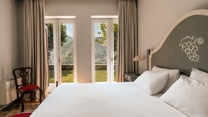 Ein Hotelzimmer mit einem großen Bett, einem Sessel mit rotem Kissen und Blick auf eine grüne Landschaft durch die Fenster.
