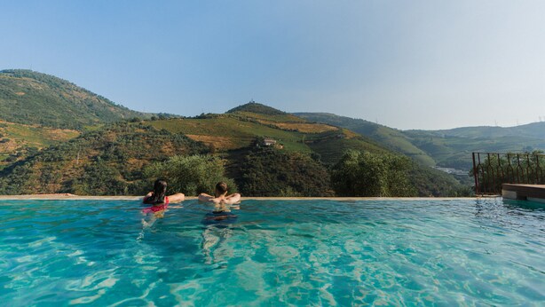 Ein Swimmingpool mit klarem, blauem Wasser, umgeben von üppigen grünen Hügeln und einem strahlend blauen Himmel.
