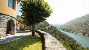Ein Steingebäude mit einer Treppe, die zu einer Tür führt, ein Baum im Vordergrund und ein Flussertal im Hintergrund.