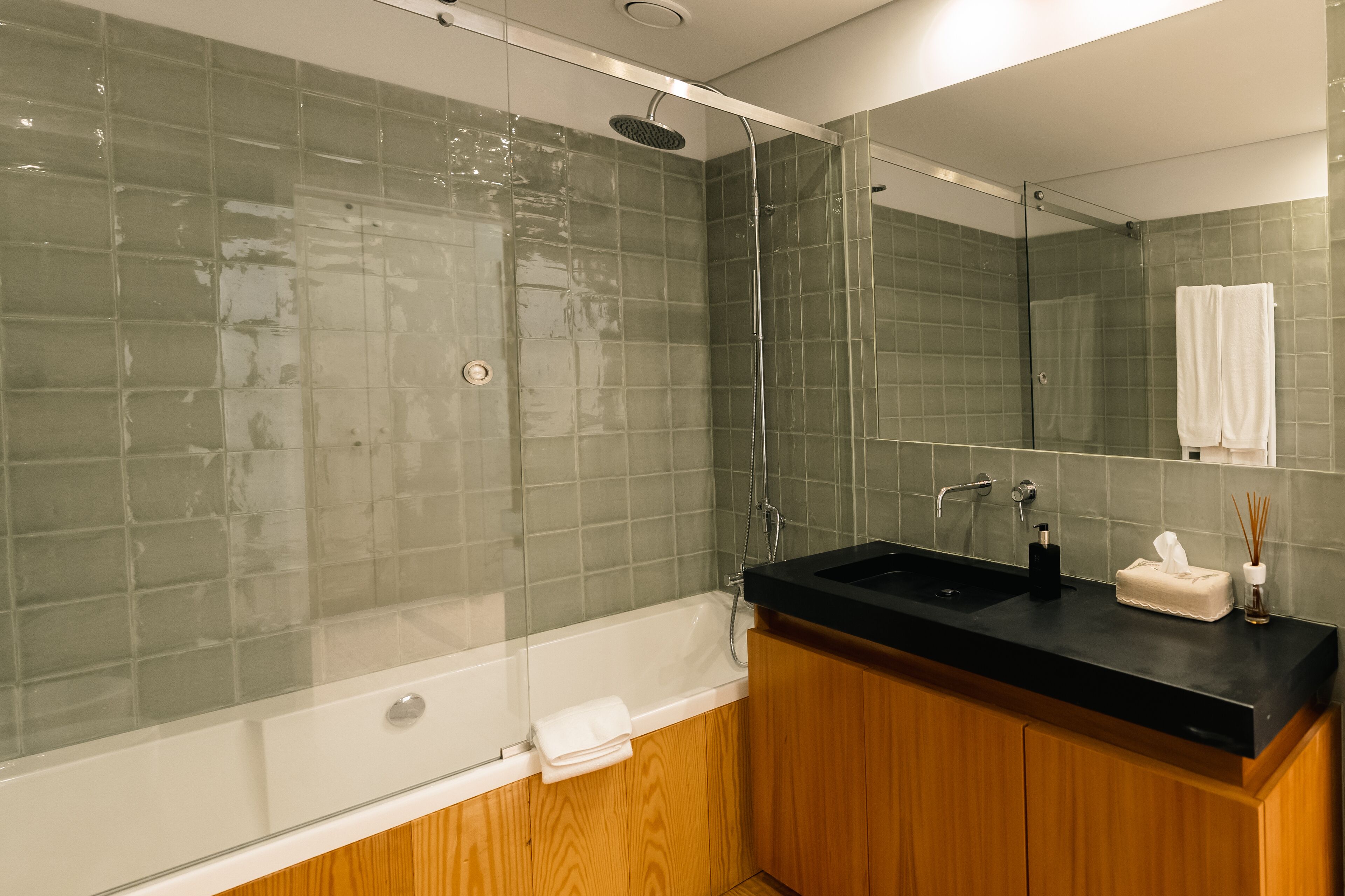 Een moderne badkamer met een douchecabine van glas, een witte badkuip en een houten wastafelmeubel met een zwart aanrecht.