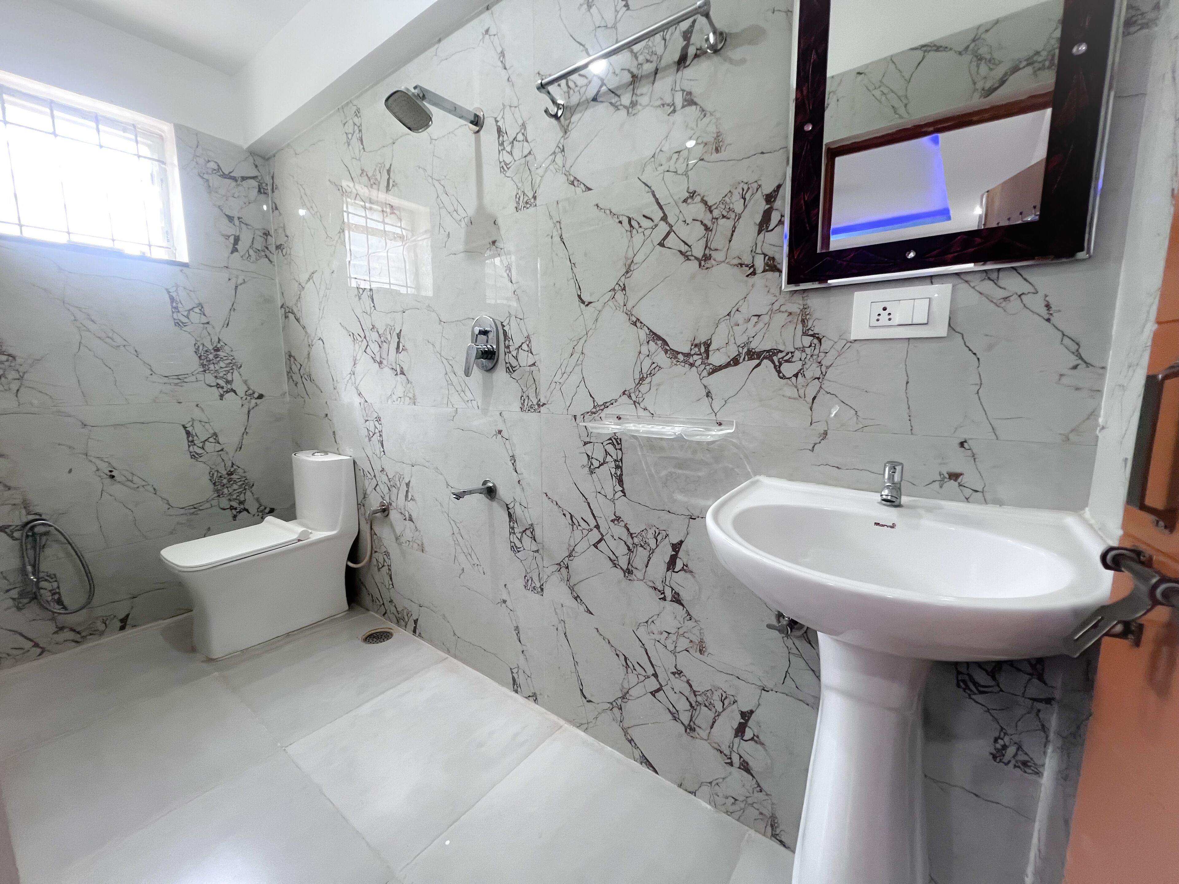 A bathroom with a marble wall, a toilet, a shower, and a sink.